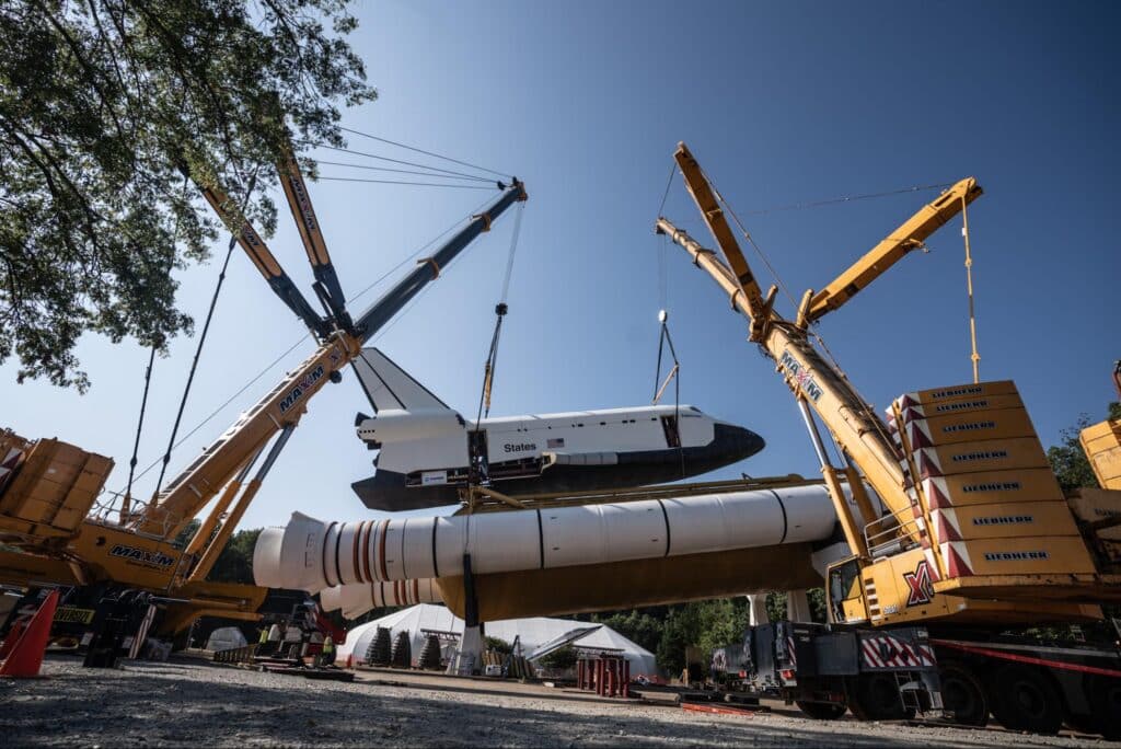Heavy cranes lifting a space shuttle during operational transport preparations.